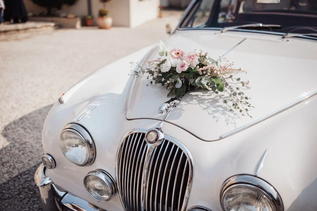 Voiture ancienne des mariés décorée d’une composition de fleurs blanches et roses