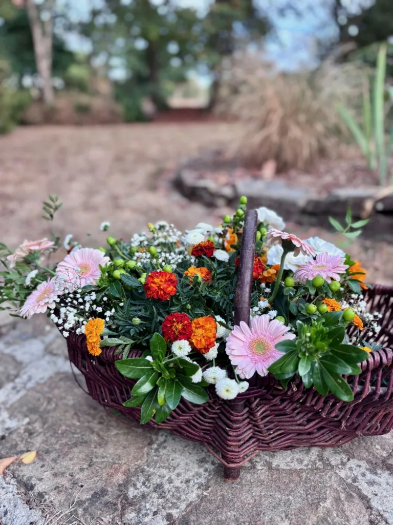 Panier en osier garni de fleurs colorées : roses, gerberas et œillets d’Inde