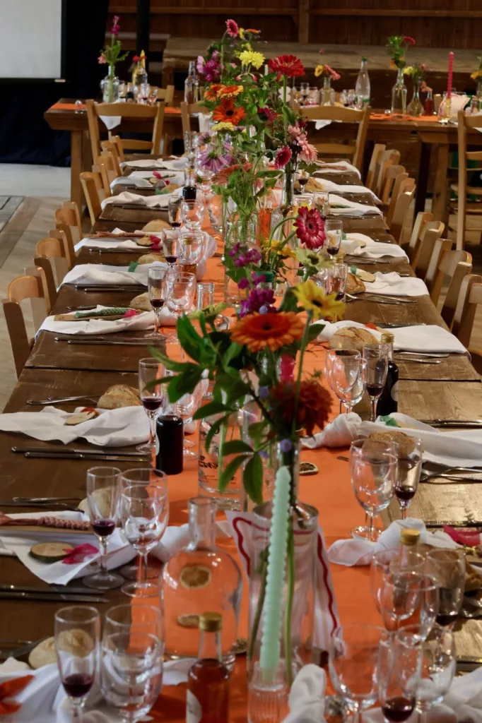 Longues tables de mariage en bois avec chemins de table orange, soliflores colorés et bougies