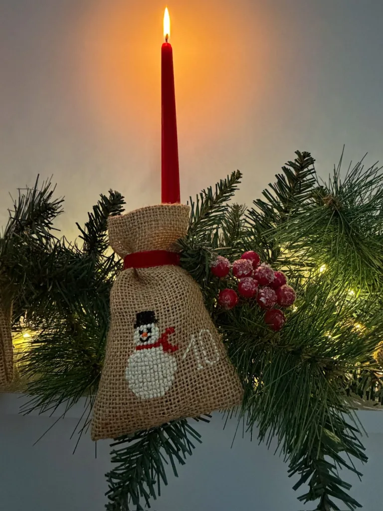 Pochon brodé au point de croix d’un bonhomme de neige, près d’une bougie de Noël