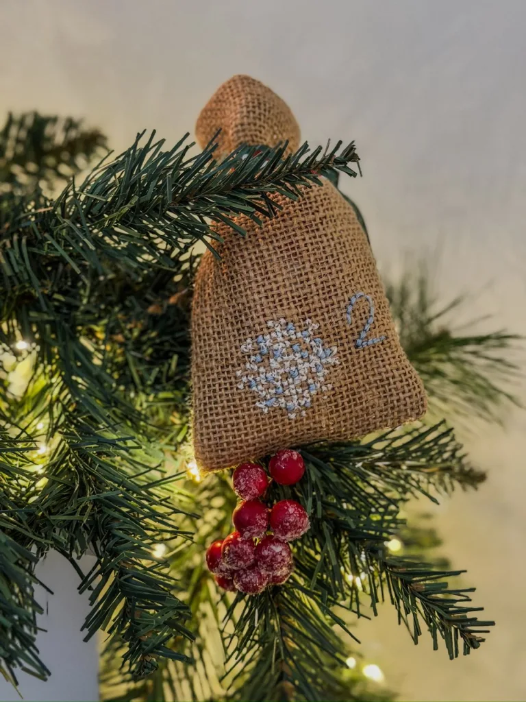 Pochon en toile de jute brodé d’un flocon, suspendu à une branche de sapin